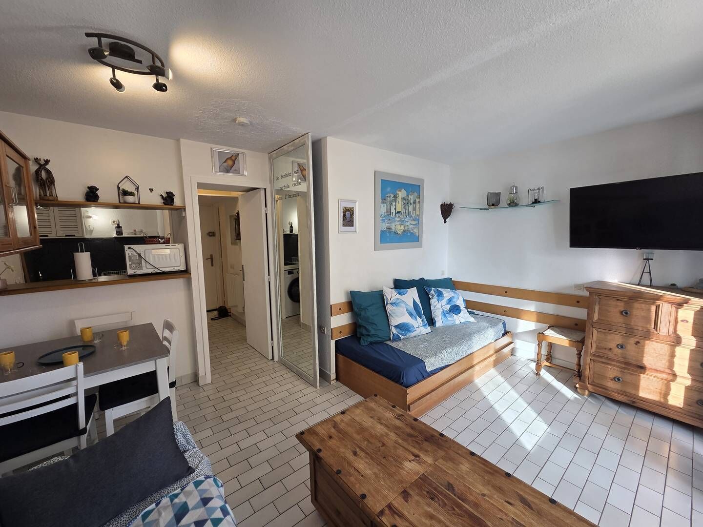Un espacio habitable compacto con kitchenette, un sofá con cojines, un aparador de madera y un televisor.