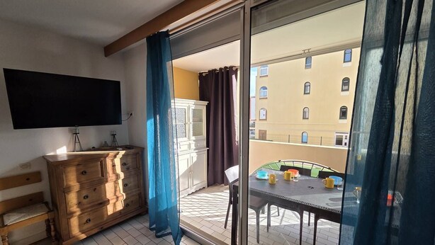 Et værelse med en trækommode, et fladskærms-tv og en skydedør af glas, der fører ud til en balkon med et bord og stole.