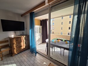 A room with a wooden dresser, a flat-screen TV, a sliding glass door leading to a balcony with a table and chairs. - Lovely studio apartment swimmingpool Richelieu beach, Cap d'Agde (LE CAP D AGDE)