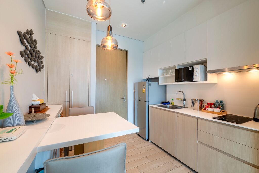 Cocina moderna con armarios de madera clara, encimera blanca, microondas integrado y pileta de acero inoxidable.