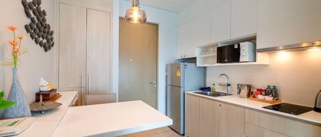 Cocina moderna con armarios de madera clara, encimera blanca, microondas integrado y pileta de acero inoxidable.