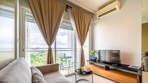 Una sala de estar moderna con un sofá, un televisor sobre un mueble de madera, y un balcón con una mesa y sillas.