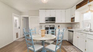 A kitchen with white cabinets, a microwave, oven, and dishwasher. There is a dining table with chairs and a rug.