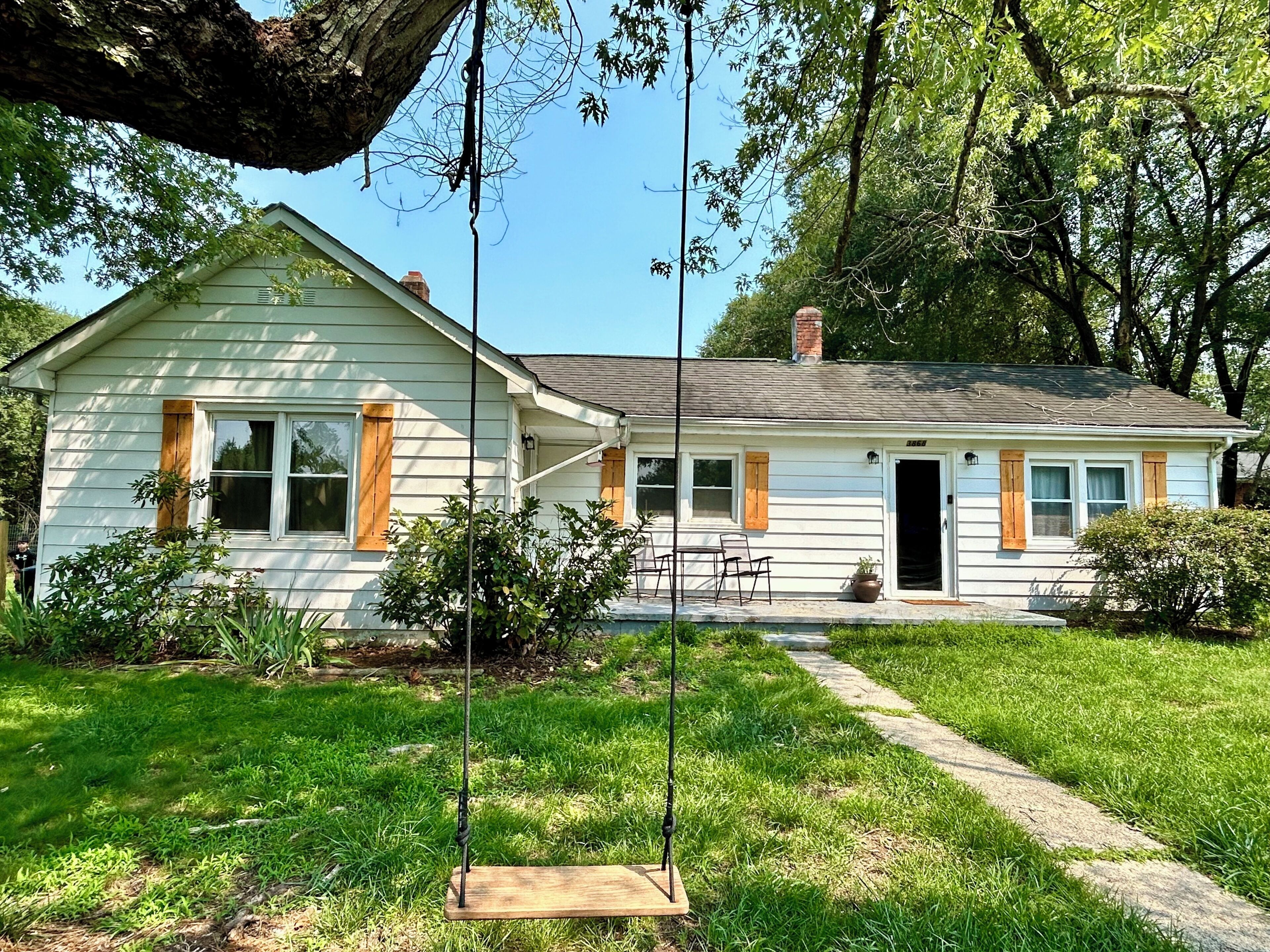 A single-story house with a front porch, a swing, and a pathway leading to the entrance.