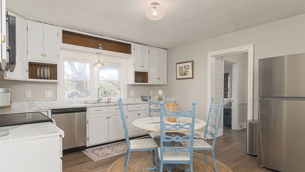 A modern kitchen with white cabinets, stainless steel appliances, and blue chairs around a round table.