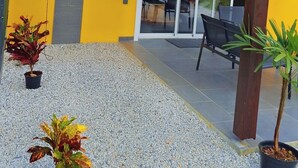 A yellow building with a patio area, a sliding glass door, and potted plants. - Emma modern suite (2-minute walk from the beach). (Kourou)