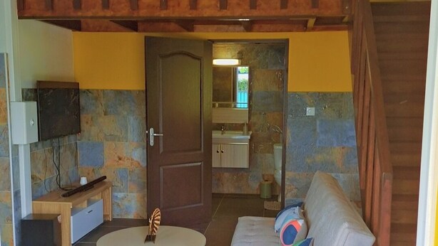 A living room with a sofa, coffee table, and a TV. There is a staircase leading to an upper level. - Emma modern suite (2-minute walk from the beach). (Kourou)
