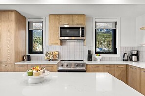Une cuisine moderne dotée d’un îlot central, d’un four à micro-ondes, d’une cuisinière et de deux fenêtres donnant sur un espace verdoyant.