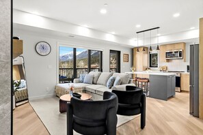 Un salon moderne comprenant un canapé, deux fauteuils, une table basse et un coin cuisine avec un réfrigérateur, un four à micro-ondes et un îlot central.