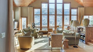 Un accogliente soggiorno con soffitto alto e ampie finestre che offrono vista su una montagna innevata. L'arredamento comprende un divano, poltrone e un tavolino.