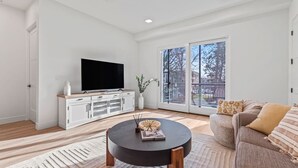 Ein modernes Wohnzimmer mit Flachbildfernseher, rundem Couchtisch und einer Couch mit gemusterten Kissen.
