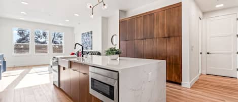 A modern kitchen with a marble island, wooden cabinets, and a built-in oven.