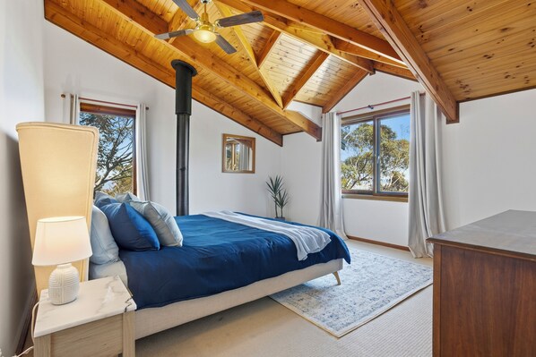 A bedroom with a bed, a nightstand, a lamp, a ceiling fan, and large windows.