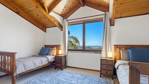 A bedroom with two beds, wooden headboards, a large window with a view, and a blue patterned rug. - Spacious Blue Mountains Retreat with Stunning Views (Mount Victoria)