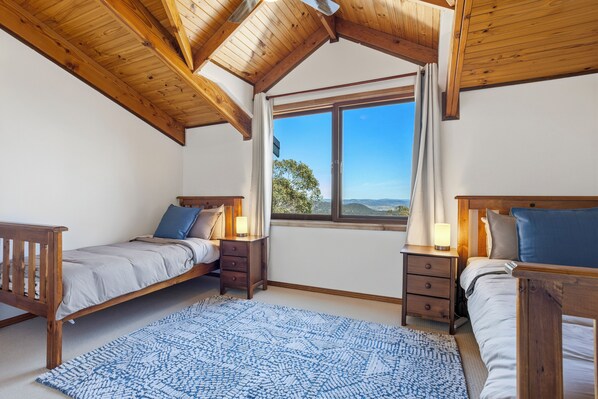 Une chambre avec deux lits, des têtes de lit en bois, une grande fenêtre donnant sur un beau paysage et un tapis bleu à motifs.