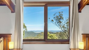 A room with a large window offering a scenic view of hills and trees. There are two bedside tables with lamps. - Spacious Blue Mountains Retreat with Stunning Views (Mount Victoria)