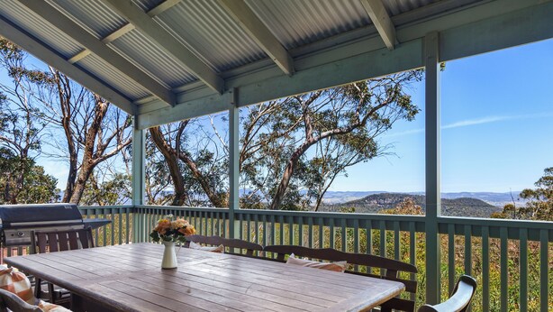 A covered outdoor dining area with a table and chairs, a grill, and a view of the surrounding landscape. - Spacious Blue Mountains Retreat with Stunning Views (Mount Victoria)