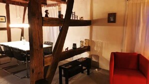 Een rustieke kamer met houten plafond, een eettafel met stoelen, een rode bank en een klein bankje.