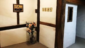 Een kamer met zichtbare houten balken, een witte muur met zwarte rand, een lijst met afbeelding en een vaas met bloemen.