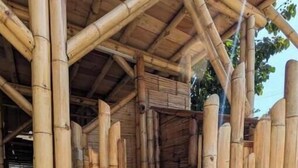 Une structure en bambou surmontée d’un toit de chaume, avec un banc en bois au centre et une base en béton.