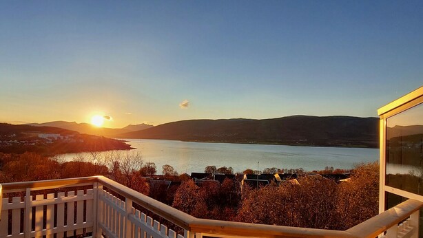 Uitzicht vanaf een balkon op een meer, met bergen op de achtergrond.