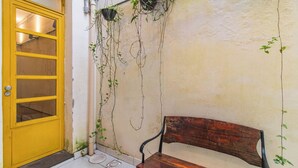Eine gelbe Tür mit Fenster, eine Holzbank und Kletterpflanzen an einer Wand.