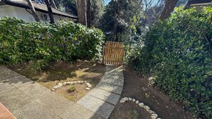 A garden pathway with a wooden fence, surrounded by lush greenery and a stone border. - Holiday flat with air conditioning and terrace (Eraclea Mare)
