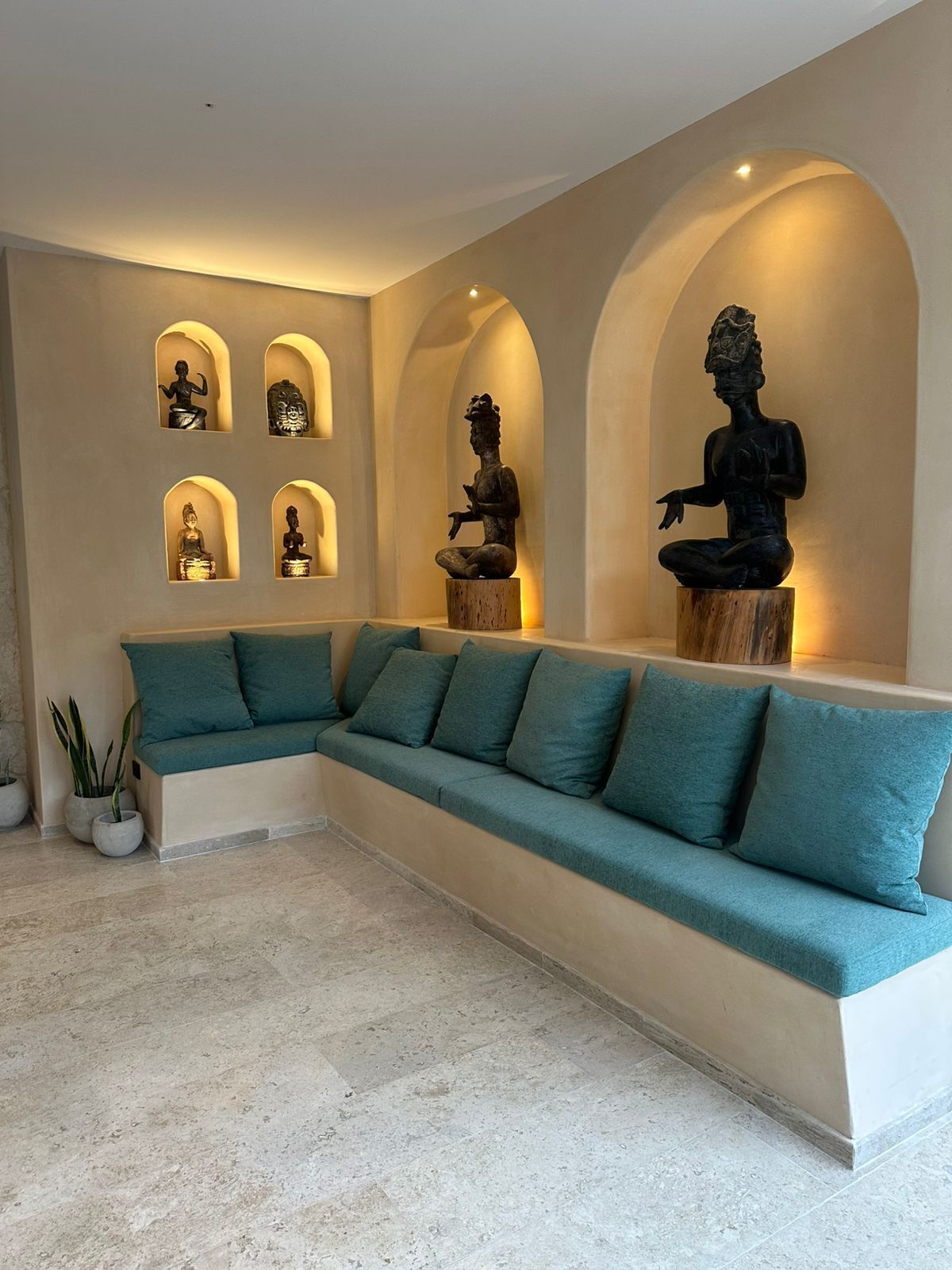 Un salon moderne avec un canapé de couleur turquoise, une table basse et un mur orné de statues.