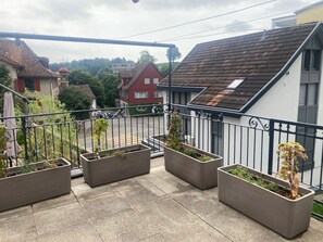 A balcony with potted plants, a view of a residential street, and houses with red roofs. - Domizil 1 by Interhome (Altstätten SG)