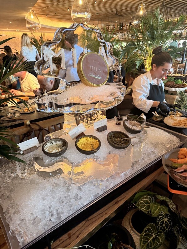 A buffet setup with various food items on ice, a person serving, and a bar area in the background. - Miami Getaway - Stadium, Beaches & Nightlife (Miami)