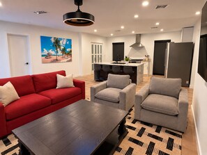 A modern living room with a red sofa, grey armchairs, and a dark wooden coffee table. - Miami Getaway - Stadium, Beaches & Nightlife (Miami)