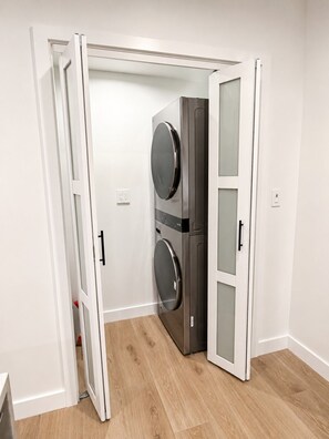 Ein Zimmer mit integrierter Waschmaschine und Trockner, einer weißen Tür und einem Holzboden.