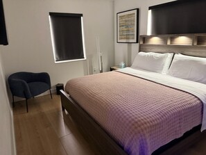 A bedroom with a bed, a chair, a bedside table, a nightstand, and a wall-mounted artwork. - Miami Getaway - Stadium, Beaches & Nightlife (Miami)