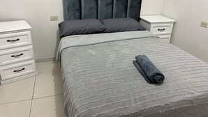 A neatly made bed with a grey bedspread and pillows, a grey upholstered headboard, and a white bedside table with drawers. - House 1 centrally located, 8 (up to 14 people) in san blas neighborhood, Comayagua (Comayagua)