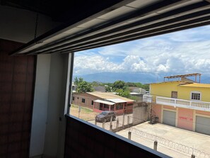 Vista desde una ventana que da a una calle con edificios, un coche y cielo despejado.