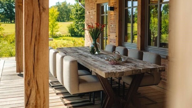 An outdoor dining area with a wooden table and benches, surrounded by a wooden deck and a covered roof structure. - Landhüüs Oeverdiek by Interhome (Niendorf)