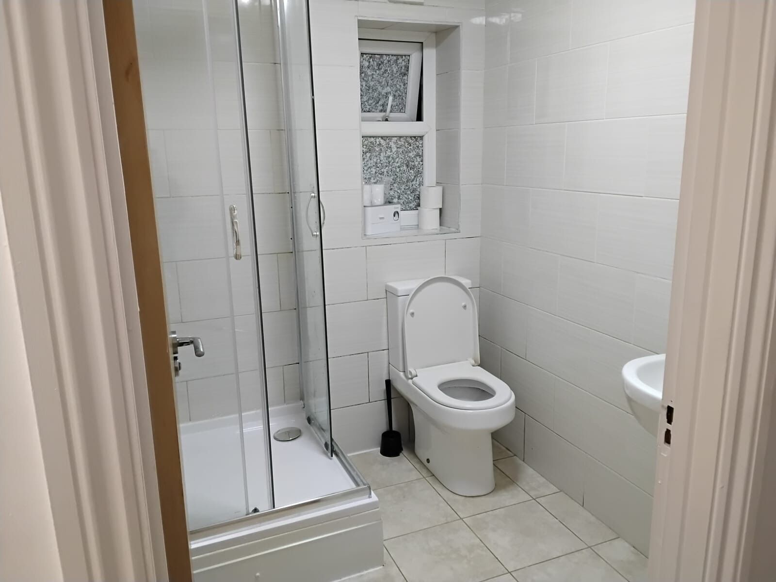 A small, clean bathroom with a toilet, a sink, and a glass-enclosed shower.