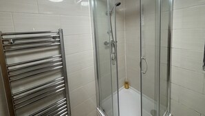 Une douche fermée par des parois en verre, équipée d’un pommeau de douche à main et d’un pulvérisateur à main.