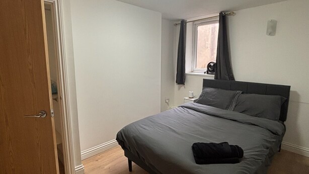 Une chambre à coucher avec un lit, une fenêtre avec des rideaux, une table de chevet et une porte.