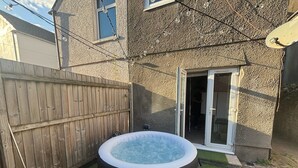 Un jardin avec un jacuzzi, une clôture en bois et une maison dotée d’une porte-fenêtre coulissante.