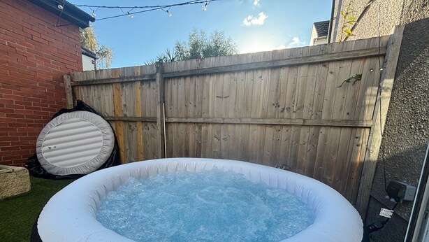 Un jacuzzi dans un jardin, avec une clôture en bois et un mur en briques.