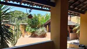 Een overdekt buitengebied met uitzicht op een binnenplaats met cactussen en palmplanten, een hangende vogelvoeder en een dakbedekking van tegels.