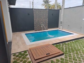 En rektangulær swimmingpool med en stenvæg og en træterrasse i forgrunden.