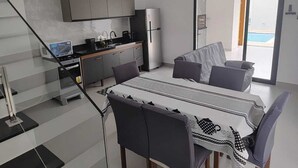 A modern kitchen with grey cabinets, a built-in oven, and a refrigerator. There is a dining area with a table and chairs, and a large window providing a view of the outside. - Refuge 1 Indaiá Beach Bertioga 150 meters from the sea (Bertioga)