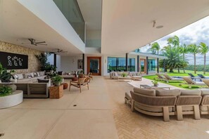 Ein großzügiger Wohnbereich mit moderner Einrichtung, einer Wand aus Stein und Blick auf einen Pool und Palmen.