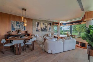 Ein modernes Wohnzimmer mit Essbereich, großen Fenstern und Blick auf Grünflächen.