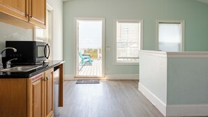 A kitchen with wooden cabinets, a black microwave, and a sink. There is a sliding glass door leading to an outdoor patio with a blue chair. - BeachDaze - Crosswalk to Beach Access, Private Pool (Panama City)