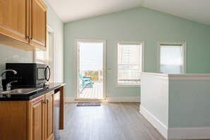 A kitchen with wooden cabinets, a black microwave, and a sink. There is a sliding glass door leading to an outdoor patio with a blue chair. - BeachDaze - Crosswalk to Beach Access, Private Pool (Panama City)
