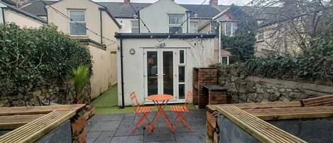 A patio with a table and chairs, a stone wall, and a house in the background.