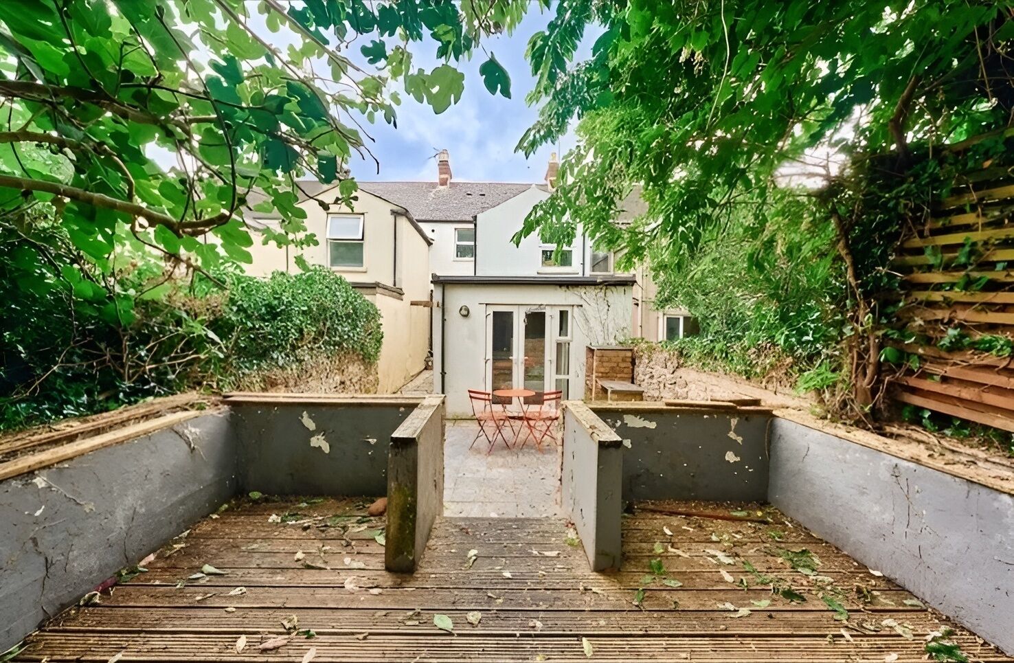 A courtyard with a wooden deck, a small table and chairs, and a concrete planter.